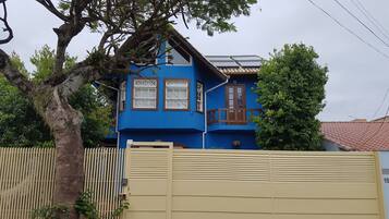 Uma casa azul com varanda, cerca de madeira e portão fechado.