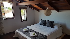 A bedroom with a wooden ceiling, a bed with white bedding, two patterned pillows, and a small window. - Solar das Pétalas (Florianópolis)