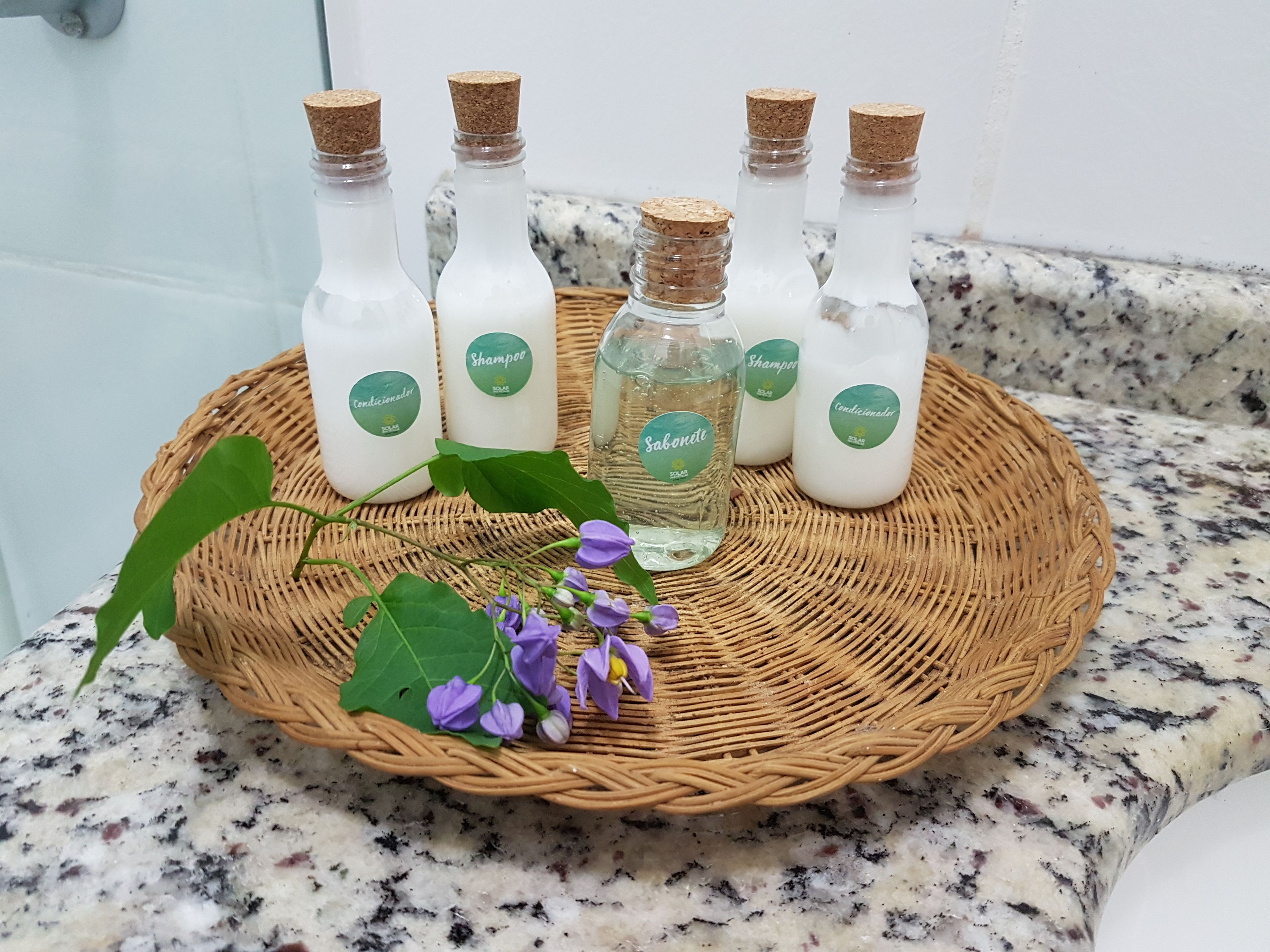 Uma bandeja de vime com garrafas de shampoo e condicionador sobre uma bancada de granito.
