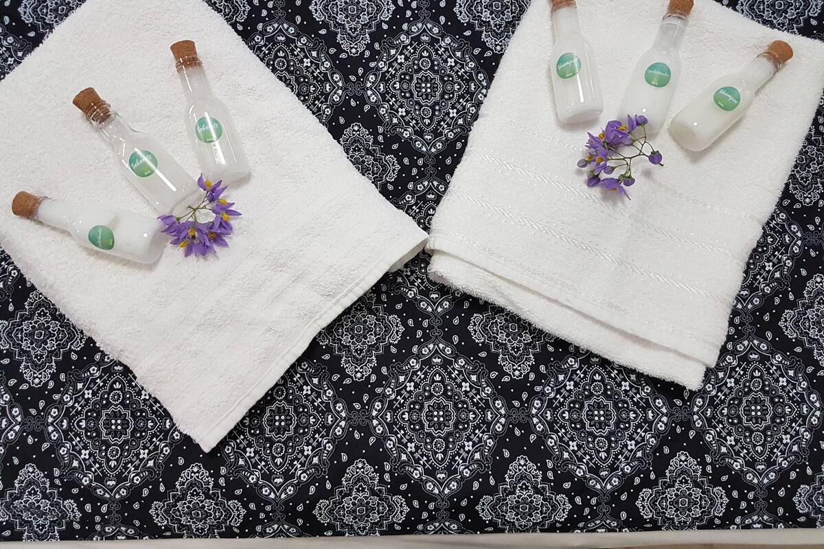 Two white towels with bottles of shampoo and purple flowers on a black patterned fabric.