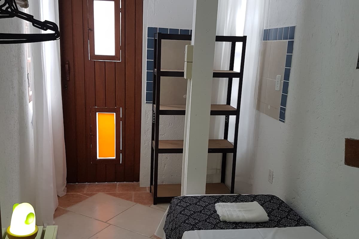 A small, clean room with a bed, a chair, a shelf, and a door.