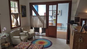 A living room with a sofa, armchairs, a coffee table, a colorful rug, and a view through a glass door to an outdoor area with a bench. - Solar das Pétalas (Florianópolis)