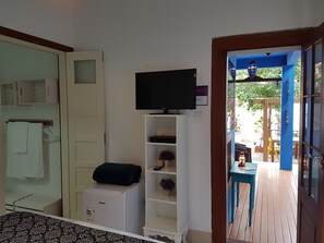 Ein Zimmer mit einem Bett, einem Fernseher auf einem Schrank, einer kleinen Kommode und einer Tür zu einem Außenbereich mit Tisch und Stühlen.
