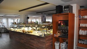 Een buffetgedeelte met een houten toonbank en een glazen vitrine, een koffieapparaat en planken met bekers en bakken.