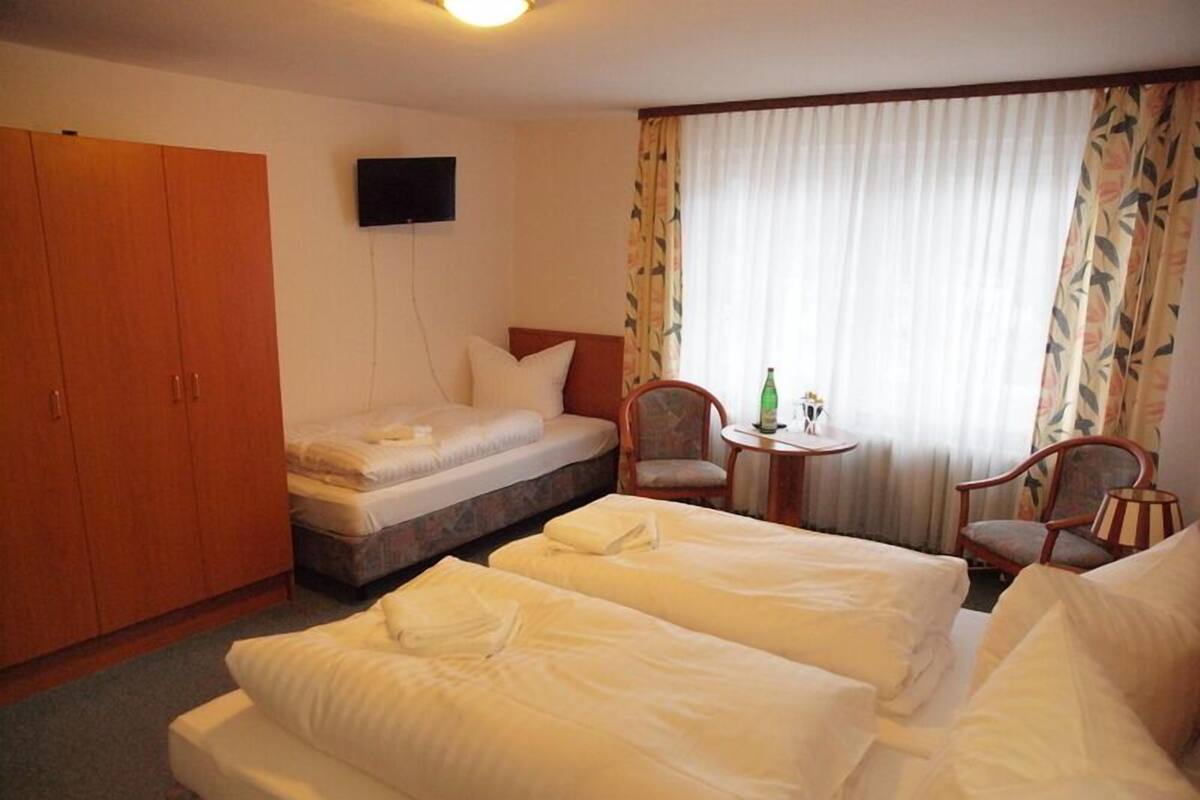 Habitación de hotel con dos camas, un armario, televisor, una mesita con una botella y una silla.