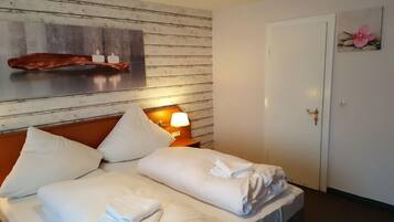 Una habitación de hotel con cabecera de madera, mesita de noche con lámpara y puerta con un llamativo ojo de cerradura.