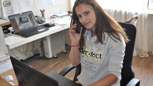 Iemand zit aan een bureau met een laptop, een desktopcomputer en papieren.
