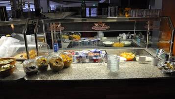 A buffet counter with various food items and containers, including bowls of fruit and containers of yogurt or dips.