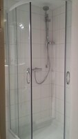 A glass-enclosed shower stall with a handheld showerhead and a wall-mounted faucet.