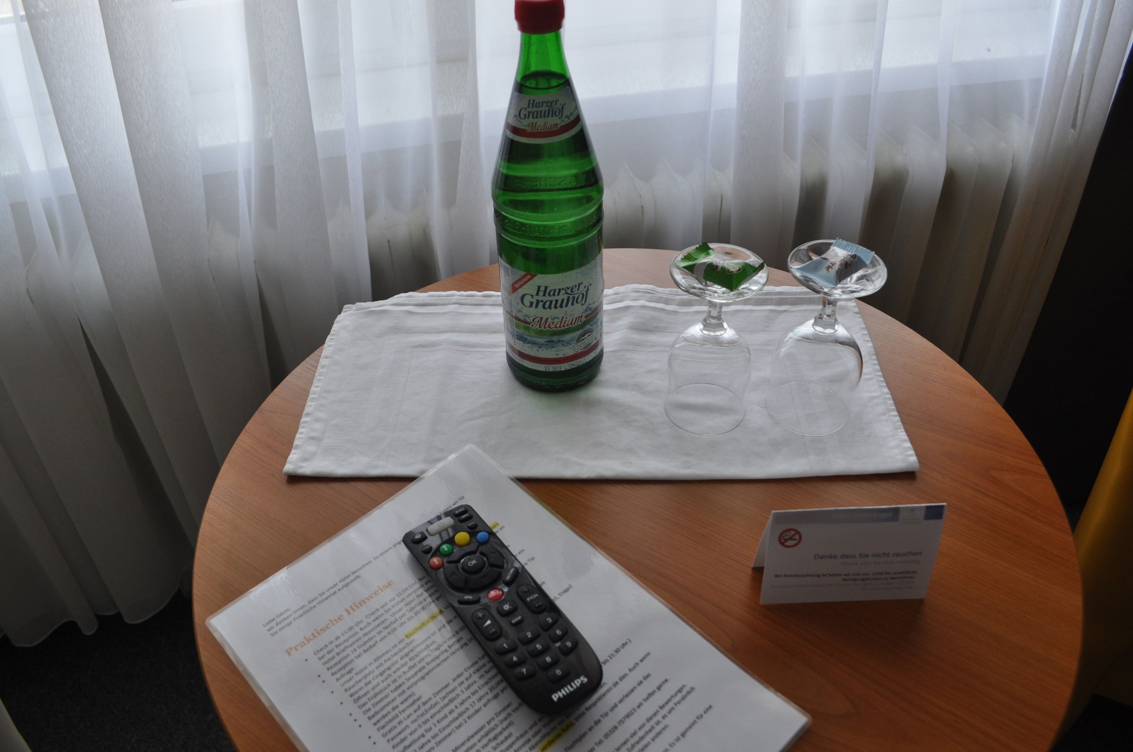 Une bouteille de Harzer Grauhaus Medium, une télécommande, un verre contenant un dessert vert et un panneau sur une table.