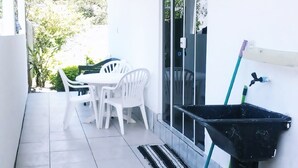 A clean, tiled balcony with a white table and chairs, a black sink, and cleaning tools. - Casa Nunes (Florianópolis)