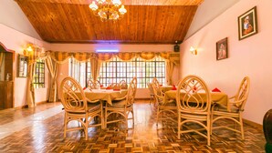 Un comedor con suelo de madera, sillas de mimbre y una araña.