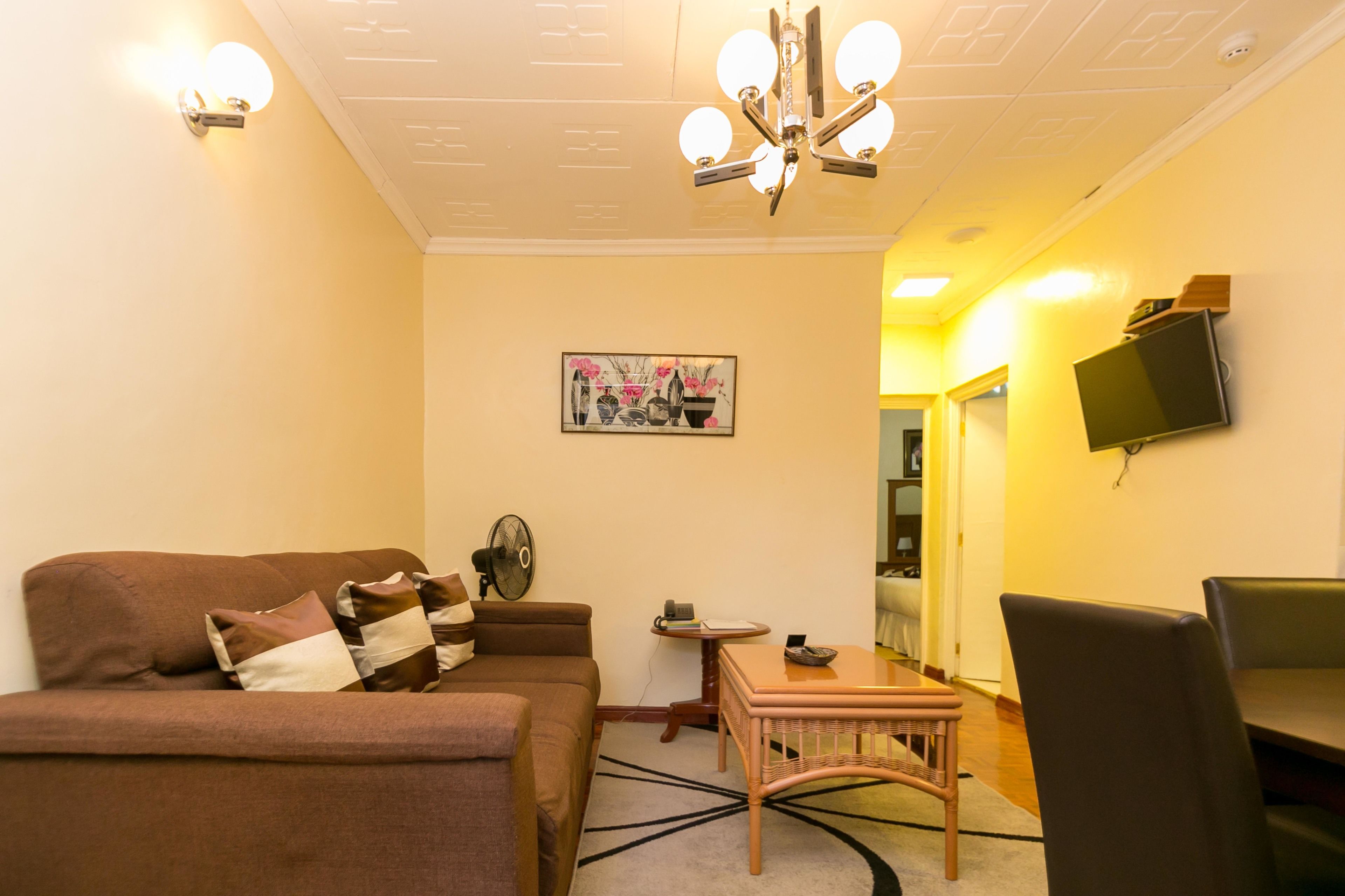 A living room with a brown sofa, a small table, and a television mounted on the wall.