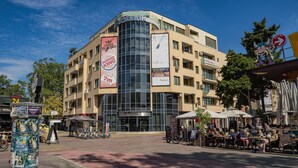 A multi-story building with a glass facade, outdoor seating area, and various commercial signs.