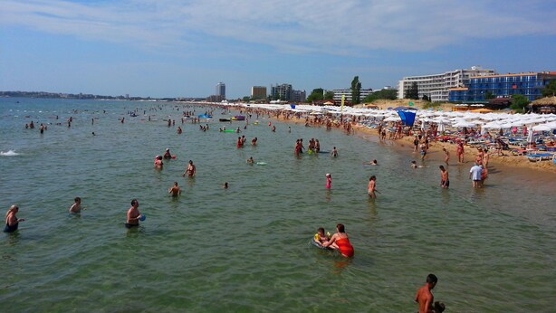 A crowded beach with people swimming and sunbathing.