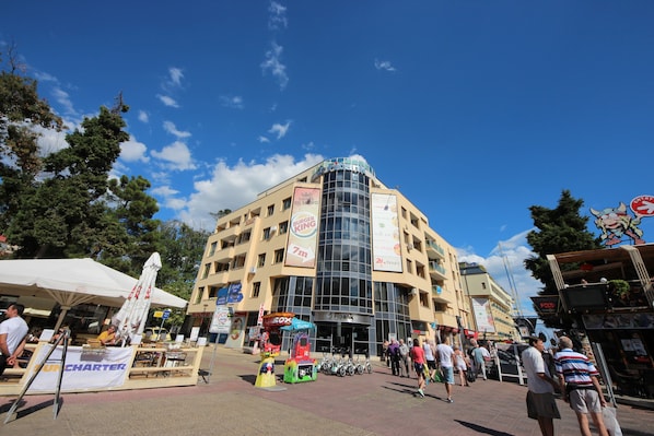 A multi-story building with a glass facade, outdoor seating area, and various commercial signs.