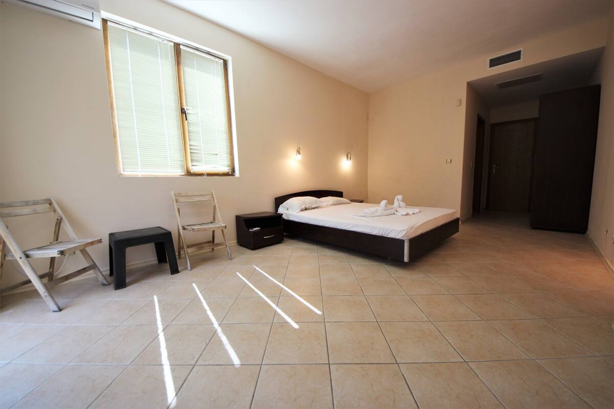 A bedroom with a bed, a nightstand, a chair, a window, and a door.