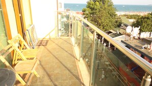 A balcony with a view of the sea and beach, glass railings, and wooden chairs.