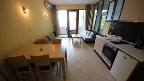 A compact living space with a dining area, sofa, kitchenette, and a sliding glass door leading to a balcony.