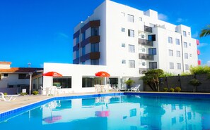 A modern building with a swimming pool, outdoor seating, and a clear blue sky.