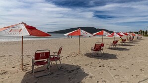 A beach with rows of red and white umbrellas and beach chairs, with footprints in the sand.