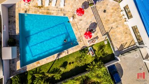 An aerial view of a swimming pool with lounge chairs and umbrellas, surrounded by a stone patio and greenery.