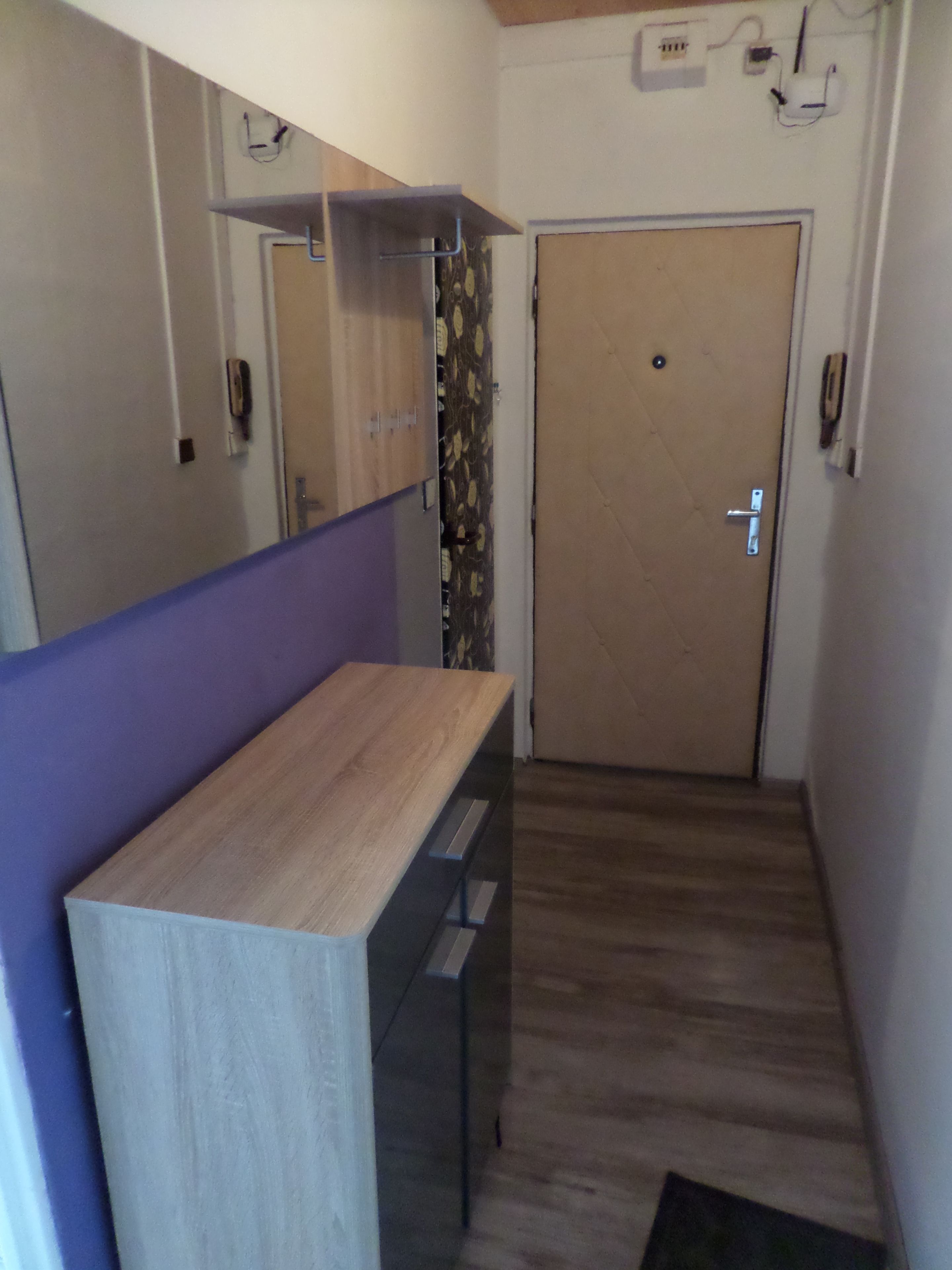 A narrow hallway with a wooden bench, a door with a handle, and a wall-mounted light fixture.