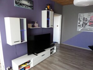 A living room with a flat-screen TV on a white entertainment unit, purple walls, and a wooden floor.
