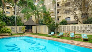 A swimming pool with lounge chairs and a gazebo, surrounded by palm trees and a fence. - Mimosa Court Apartments (Nairobi)