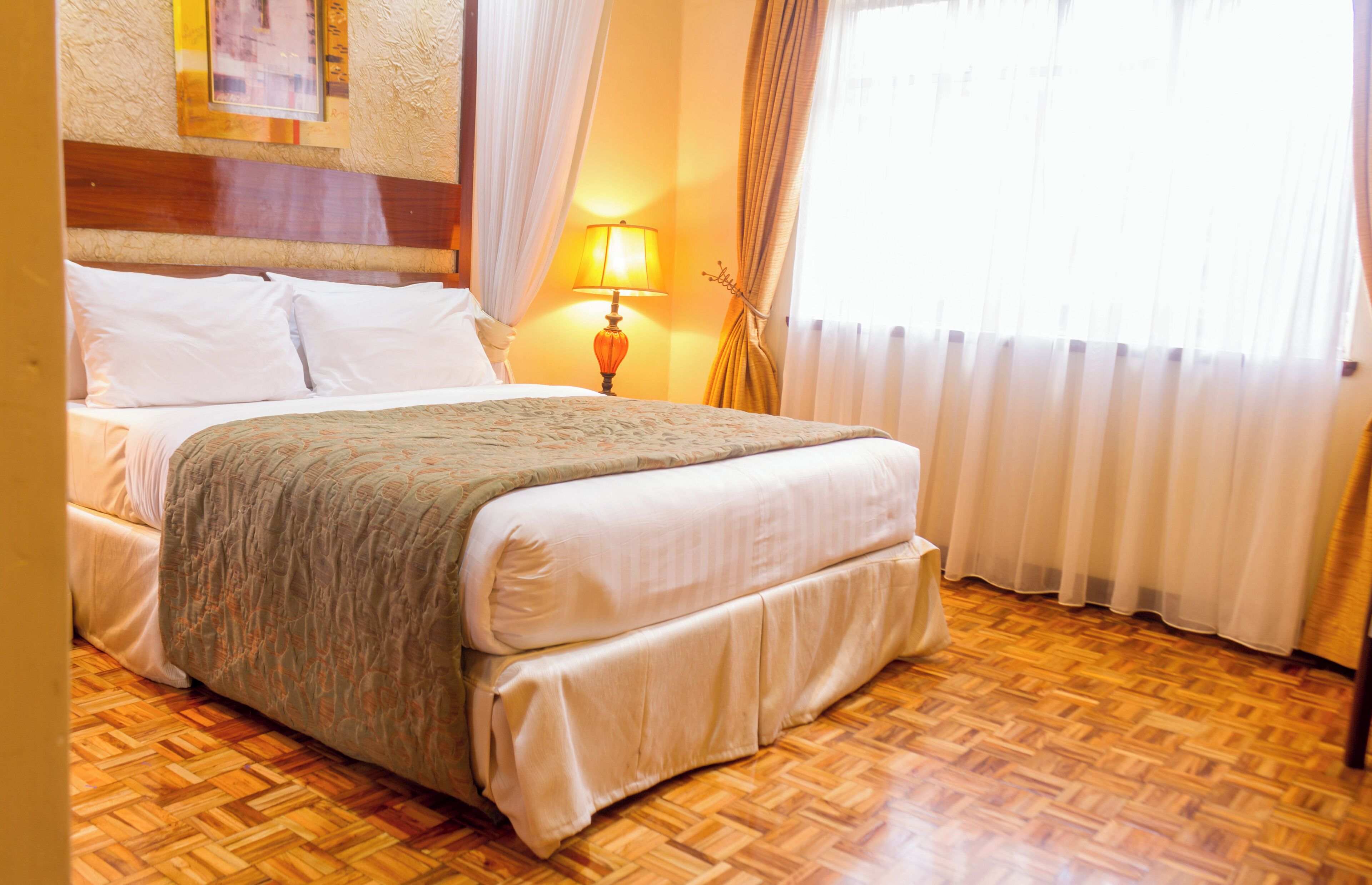 A hotel room with a large bed, wooden flooring, and a window with curtains.
