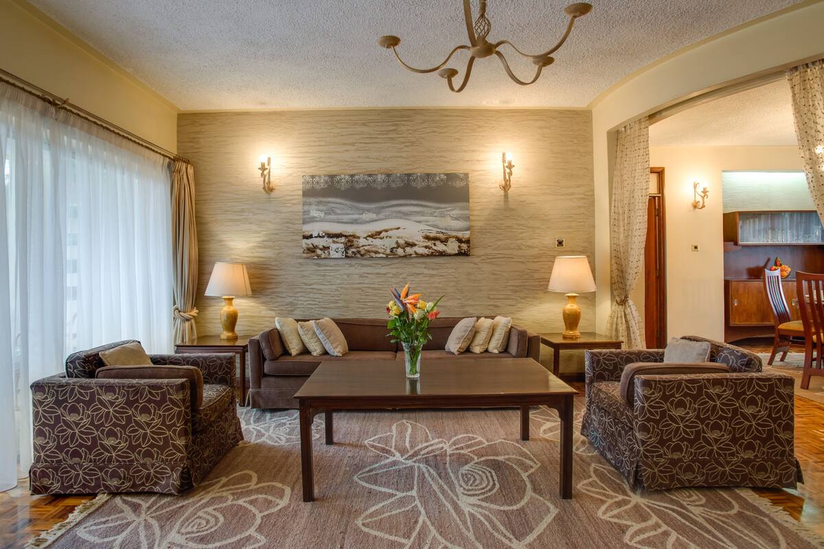 A living room with a sofa set, a coffee table, and two lamps. There is a painting on the wall and a chandelier.