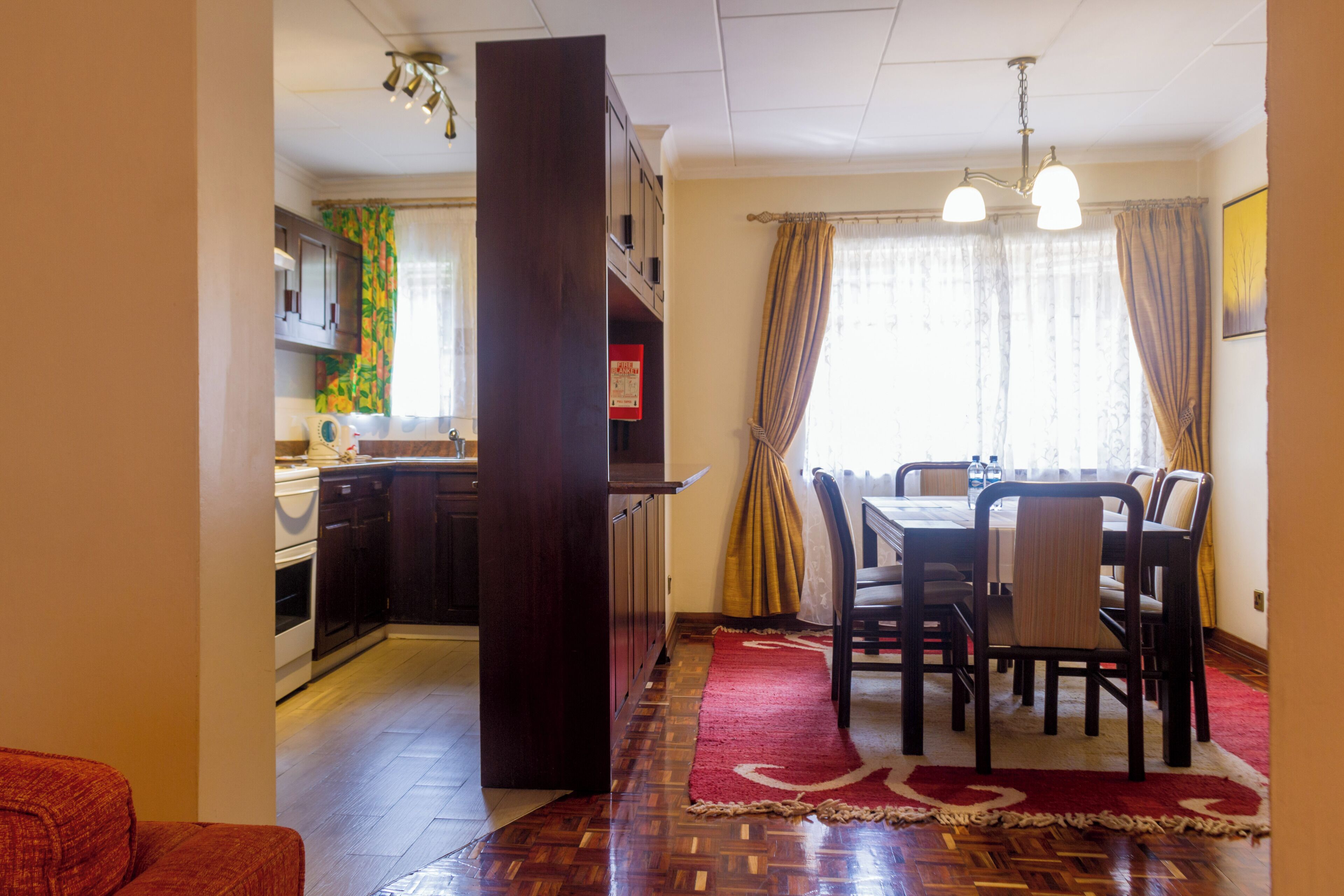 A kitchen with dark cabinets, a dining area with a table and chairs, and a red rug.