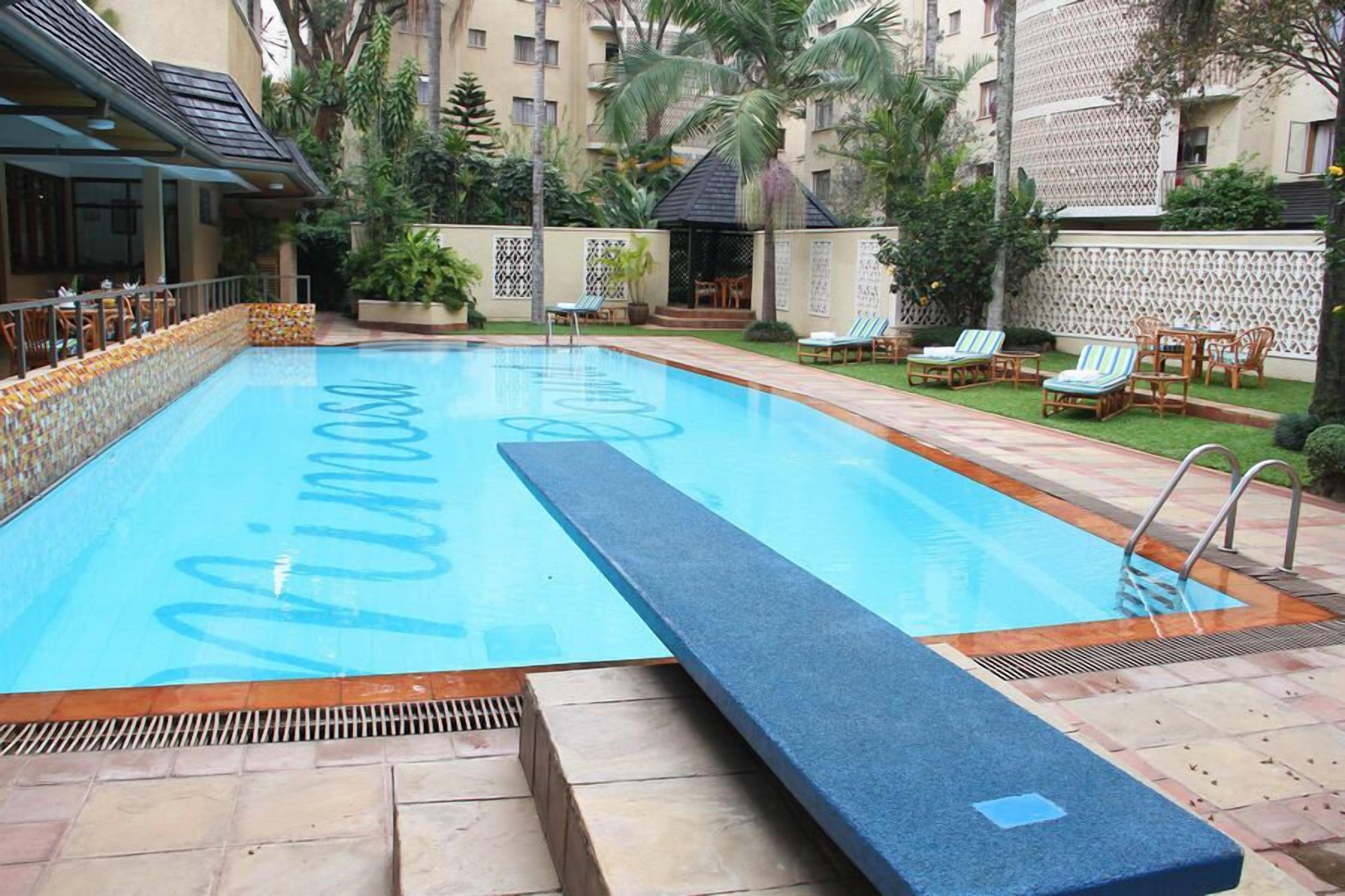 A swimming pool with a tiled edge and a blue border, surrounded by lounge chairs and a covered seating area.