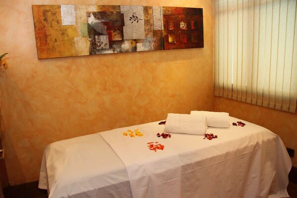 A neatly made bed with white linens and a towel, a wall art piece above it, and a window with blinds.