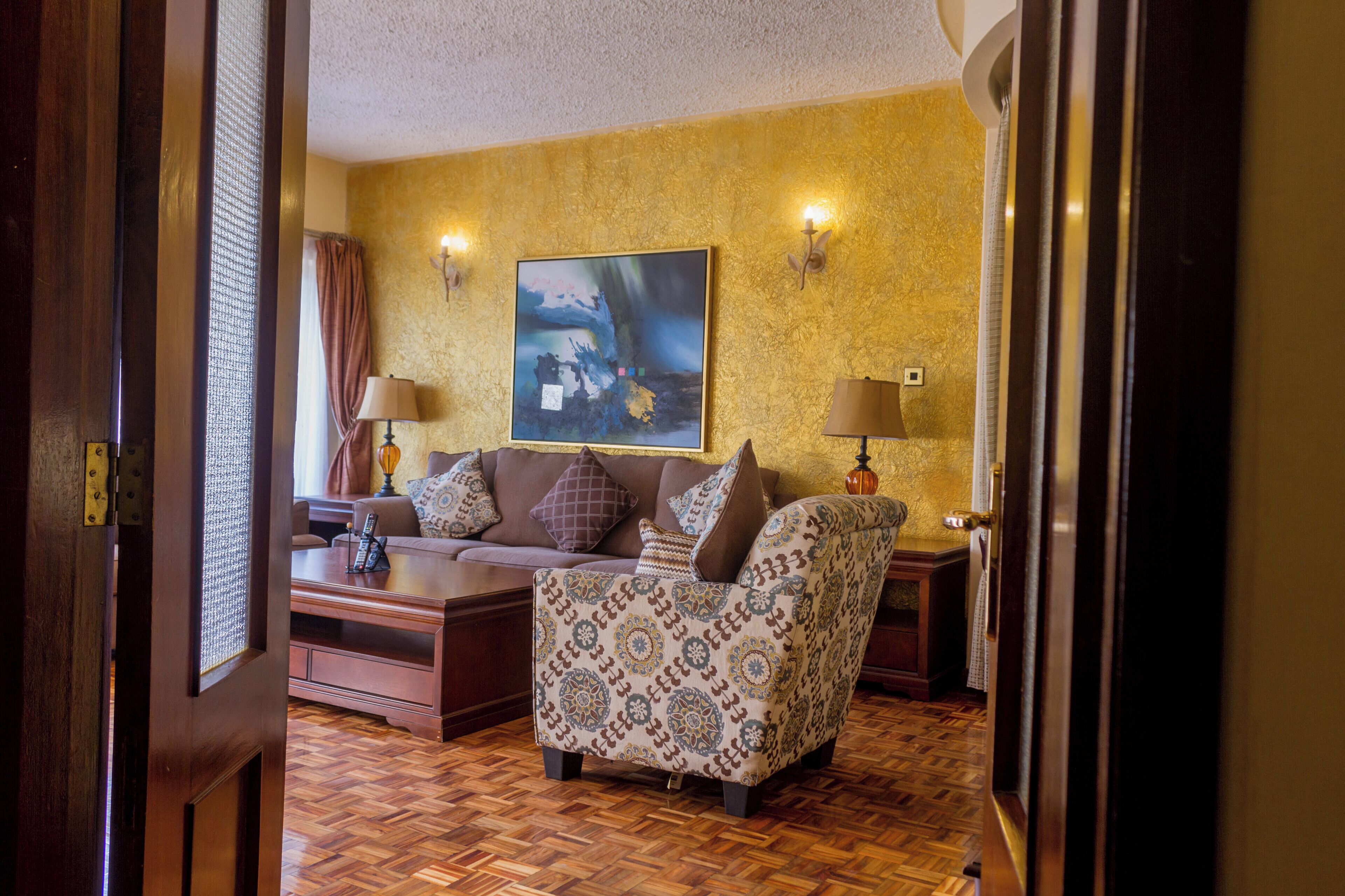 Una habitación con un sillón estampado, un sofá y una mesita de centro. Hay un cuadro en la pared y dos lámparas a cada lado del sofá.