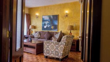 Una habitación con un sillón estampado, un sofá y una mesita de centro. Hay un cuadro en la pared y dos lámparas a cada lado del sofá.