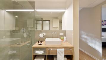 Un baño moderno con cabina de ducha de vidrio, tocador de madera con un lavabo grande y un espejo.