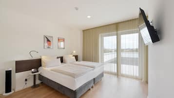 A modern hotel room with a large bed, a flat-screen TV mounted on the wall, and a balcony with a view.