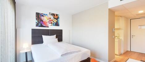 A hotel room with a bed, a nightstand, a chair, and two paintings on the wall.