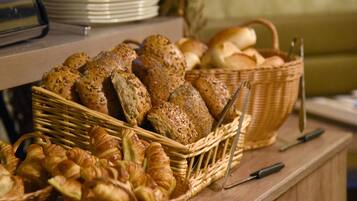 A variety of breads and pastries displayed in wicker baskets on a wooden counter.
