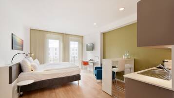 Una habitación de hotel moderna con una cama grande, un escritorio, una kitchenette y un televisor.