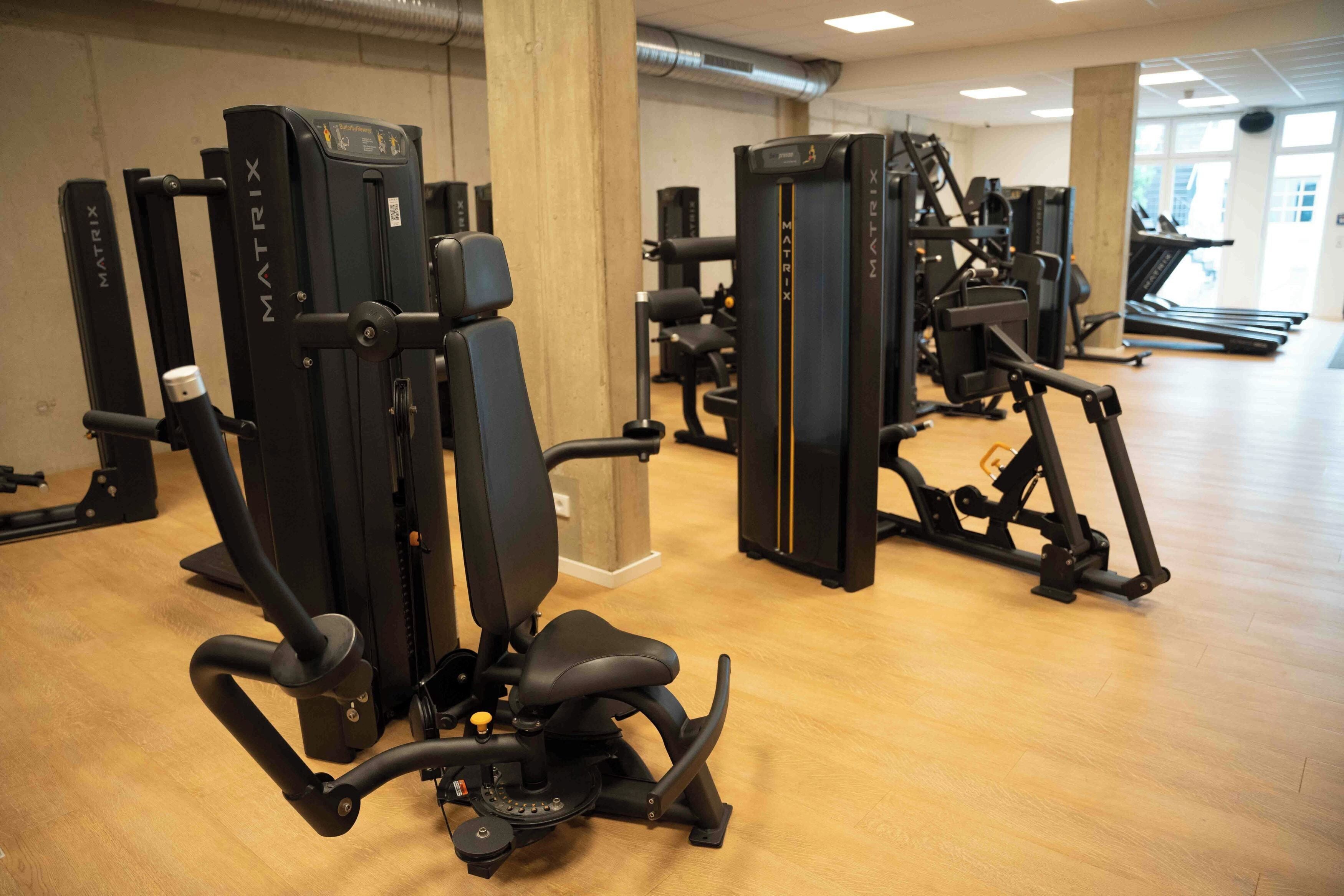 A gym with multiple exercise machines, a treadmill, and a wooden floor.