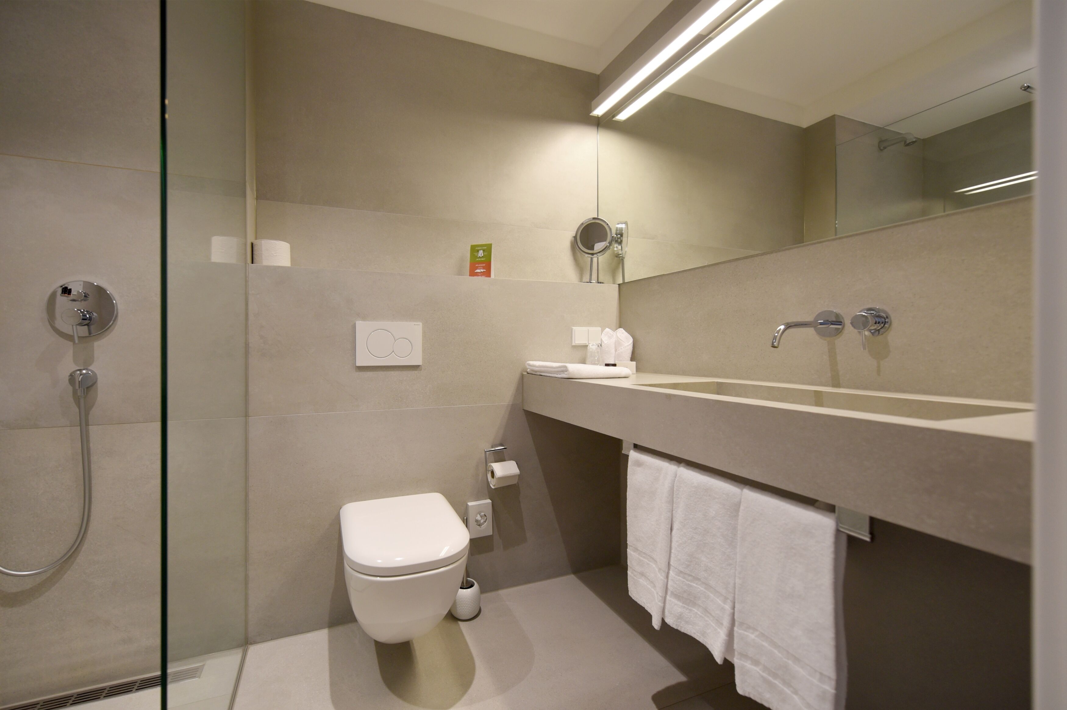 Une salle de bain moderne avec une douche à parois de verre, des toilettes, un lavabo avec un miroir et un porte-serviettes.