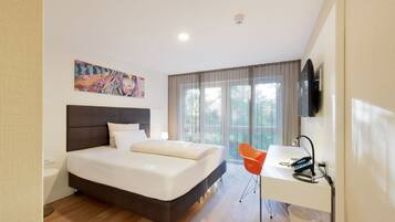 A modern hotel room with a large bed, a desk with a chair, a flat-screen TV, and a window with curtains.