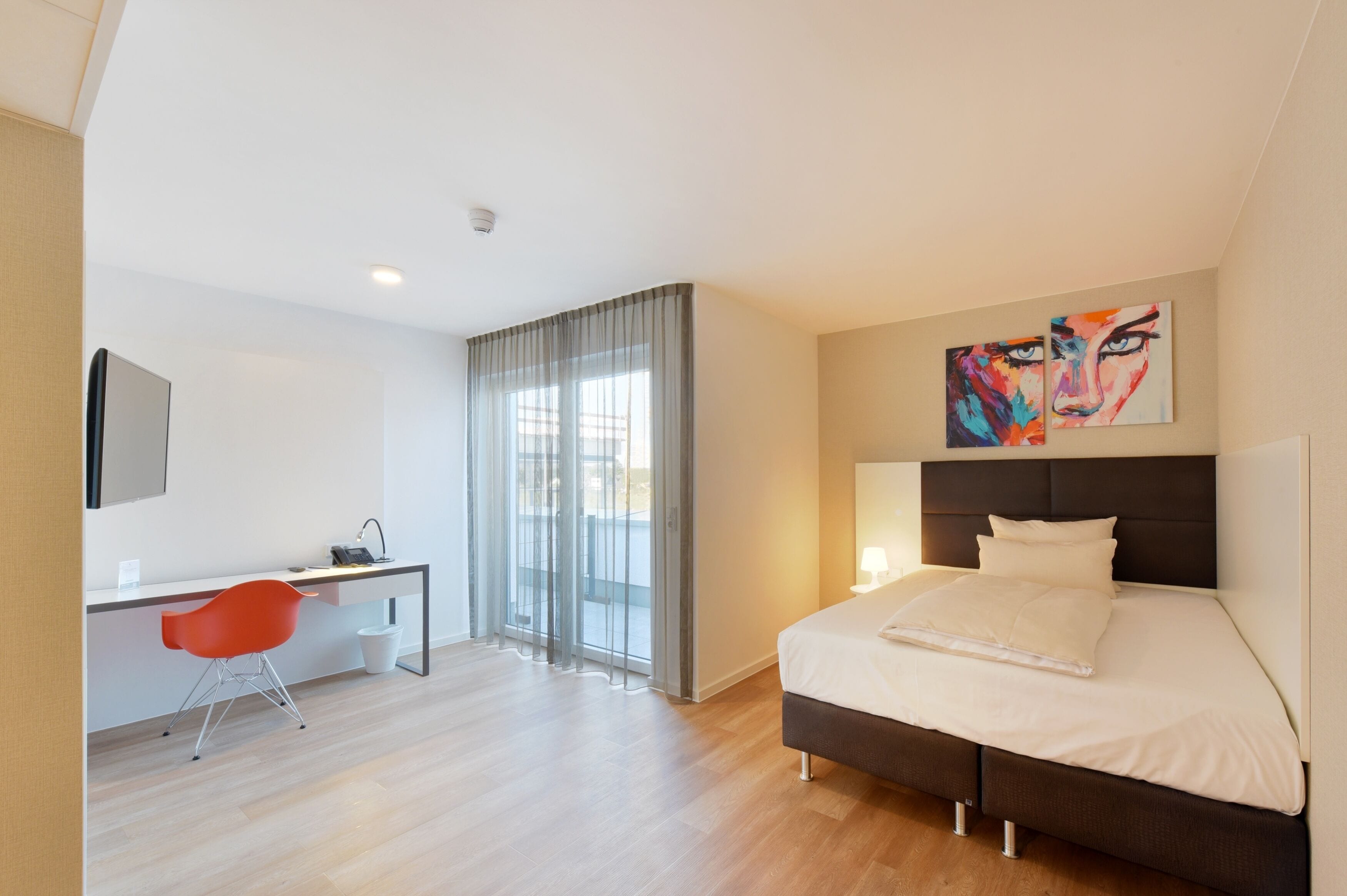 Una habitación de hotel moderna con una cama, un escritorio, una silla y un ventanal con cortinas.
