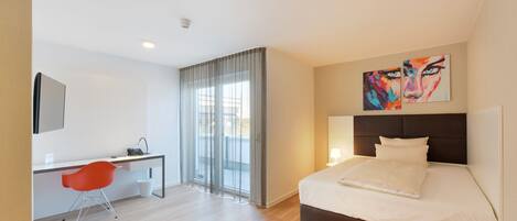 Una habitación de hotel moderna con una cama, un escritorio, una silla y un ventanal con cortinas.