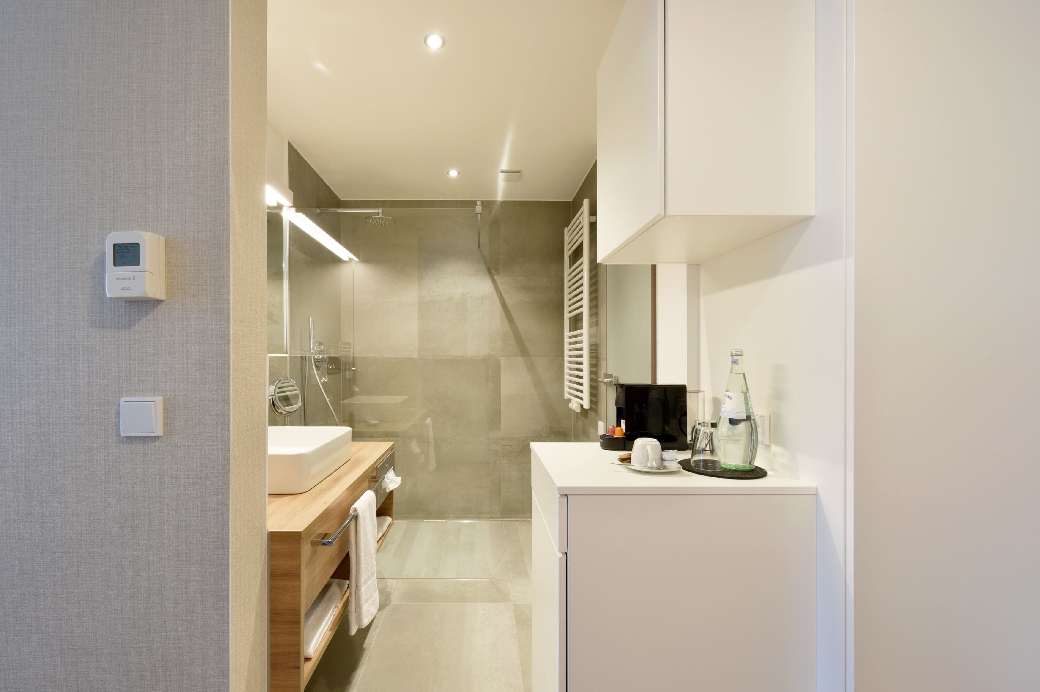 A modern bathroom with a glass shower, a white sink, and a coffee maker on the counter.
