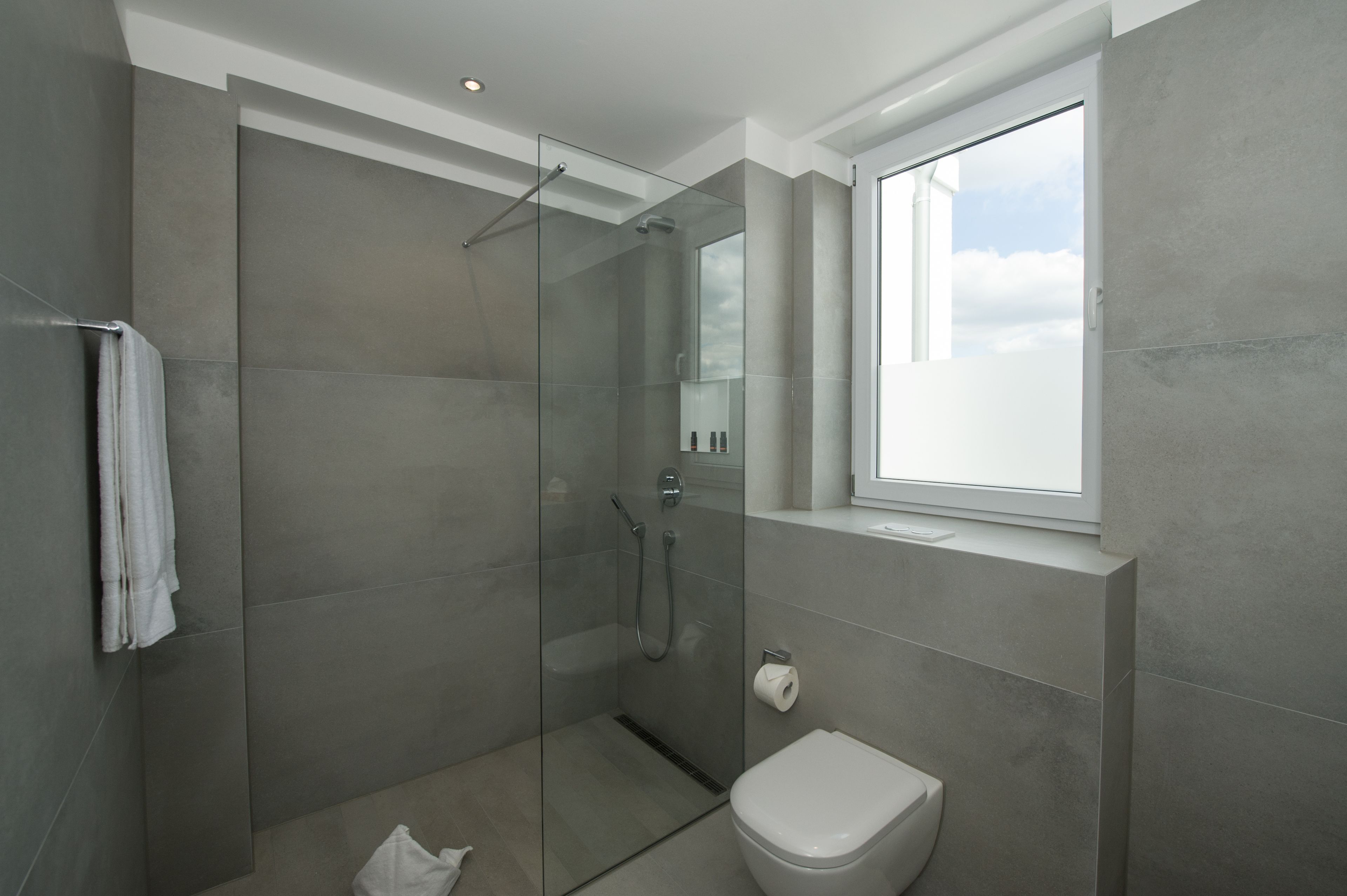 Un baño moderno con ducha de vidrio, inodoro y ventana que proporciona luz natural.
