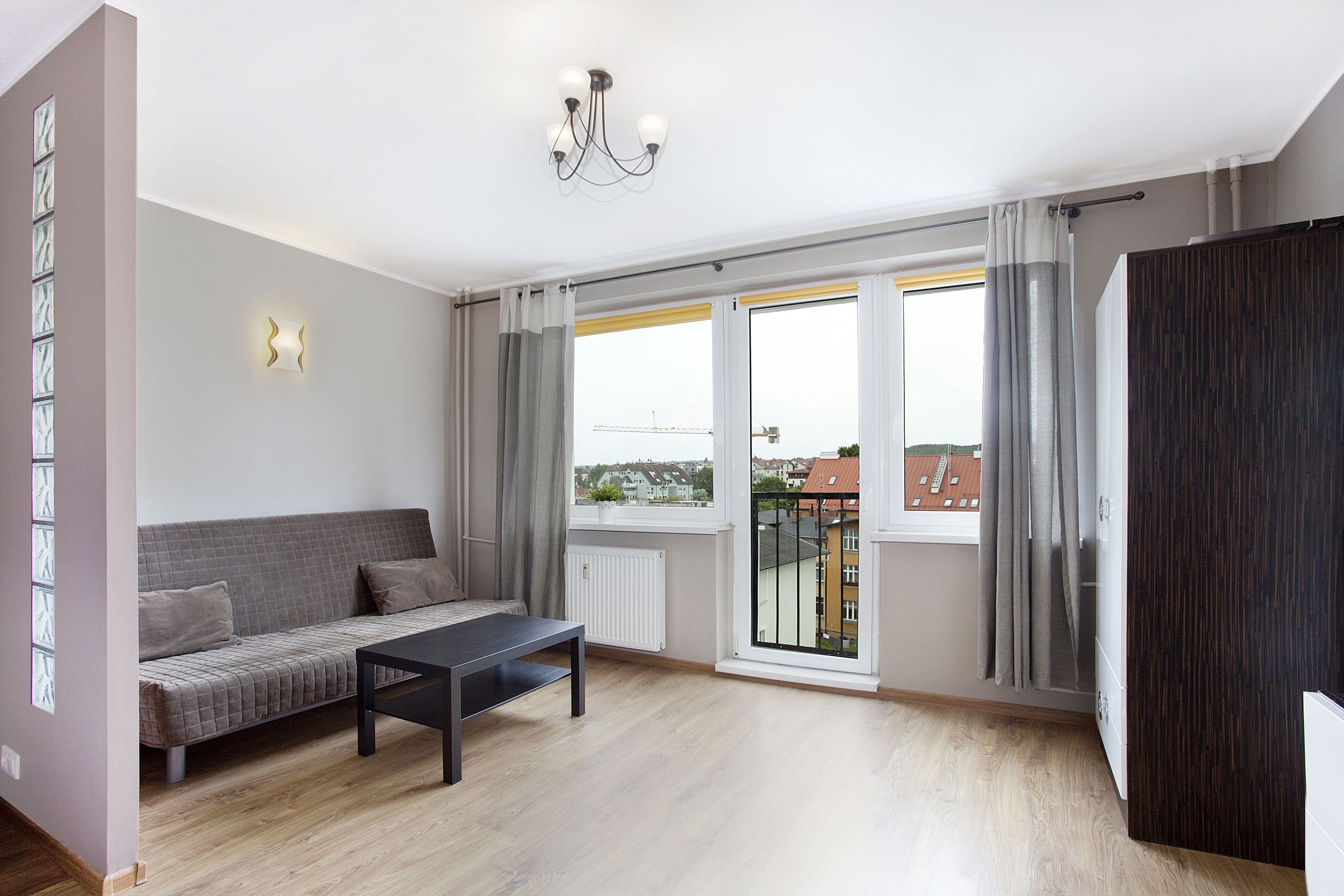 A modern living room with a sofa, a coffee table, and a view of the city through large windows.