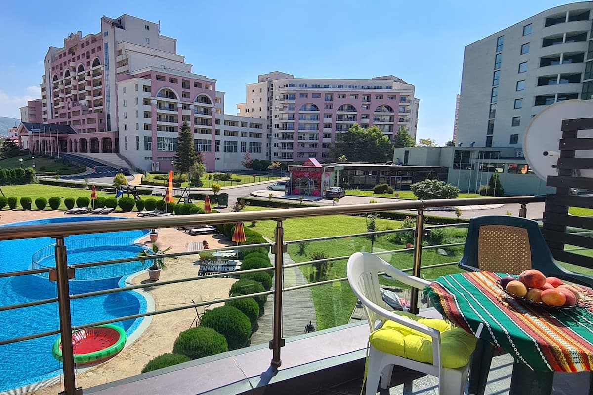 Un balcon d’hôtel avec une piscine, des chaises longues et une table où sont disposés des fruits.